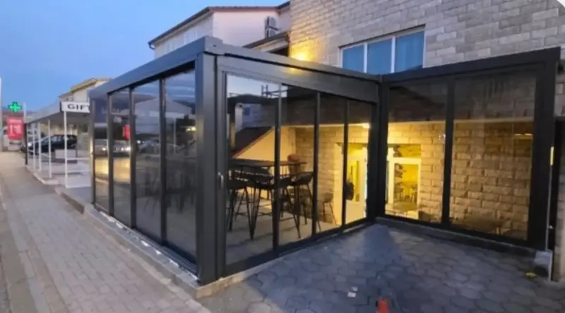 Ostakljena bašta kafića u crnim aluminijskim profilima, uveče
