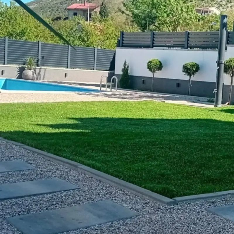 Dvorište s travnjakom i bazenom, ograđeno tamnom alu ogradom