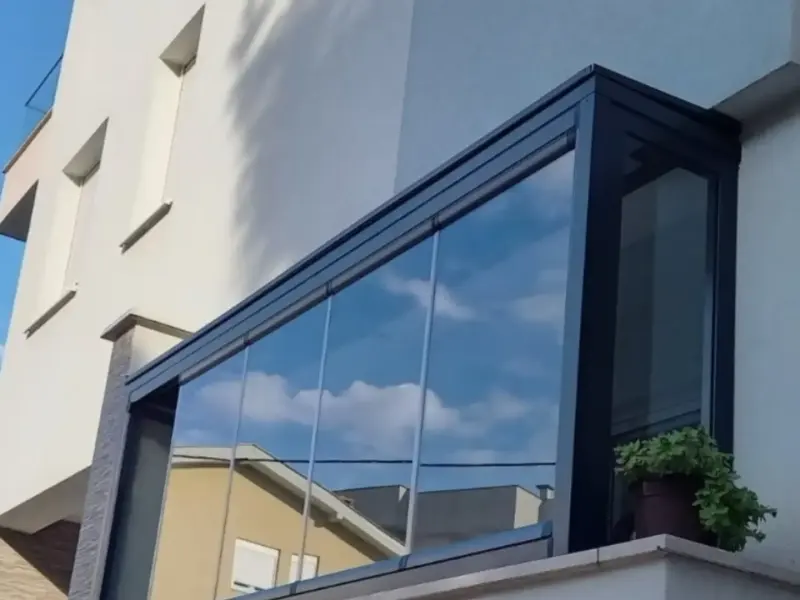 Ostakljen balkon na fasadi kuće, staklena krila u tamnom aluminijskom okviru