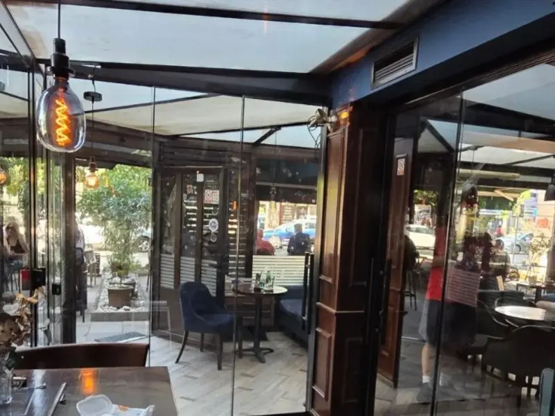 Bašta kafića zatvorena staklenim kliznim stijenama, stolovi uz staklo